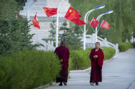 Monks walk along a sidewalk path lined with Chinese flags at the Tibetan Buddhist College near Lhasa in western China's Tibet Autonomous Region, Monday, May 31, 2021, as seen during a government organized visit for foreign journalists. High-pressure tactics employed by China's ruling Communist Party appear to be finding success in separating Tibetans from their traditional Buddhist culture and the influence of the Dalai Lama. (AP Photo/Mark Schiefelbein)