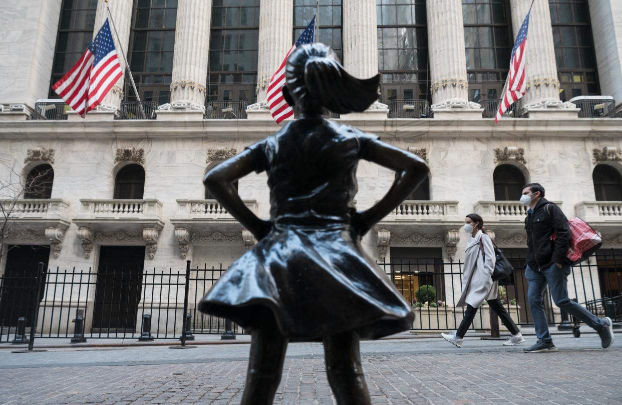 People walk past the New York Stock Exchange (NYSE) at Wall Street and the  'Fearless Girl' statue on March 23, 2021 in New York City. - Wall Street stocks were under pressure early ahead of congressional testimony from Federal Reserve Chief Jerome Powell as US Treasury bond yields continued to retreat. (Photo by Angela Weiss / AFP) (Photo by ANGELA WEISS/AFP via Getty Images)