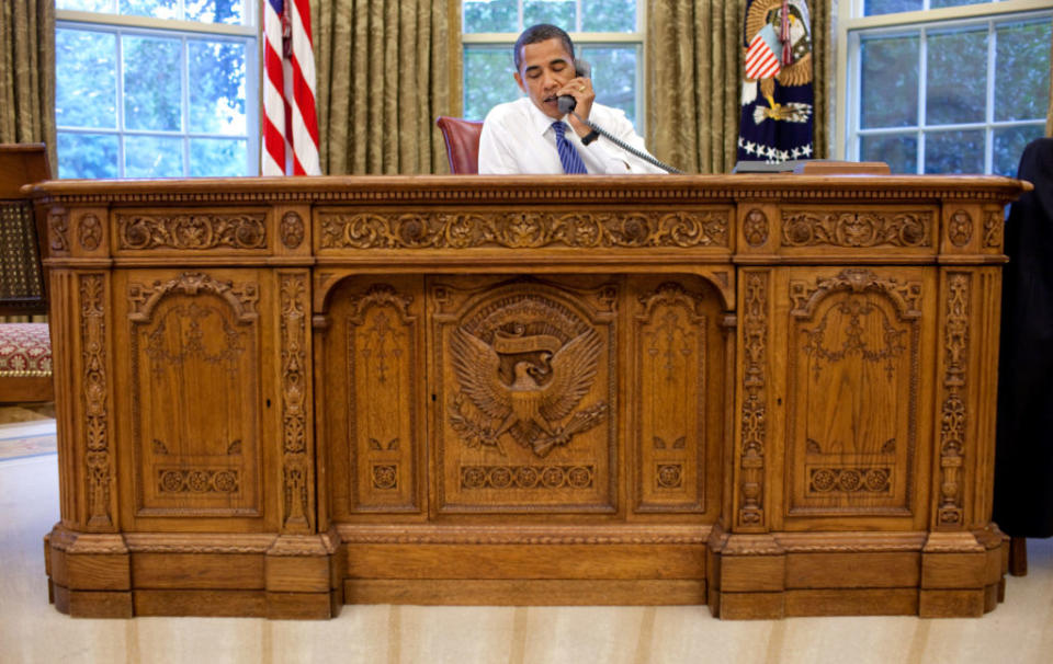 President Barack Obama takes a conference call while sitting behind the Resolute Desk in the Oval Office.