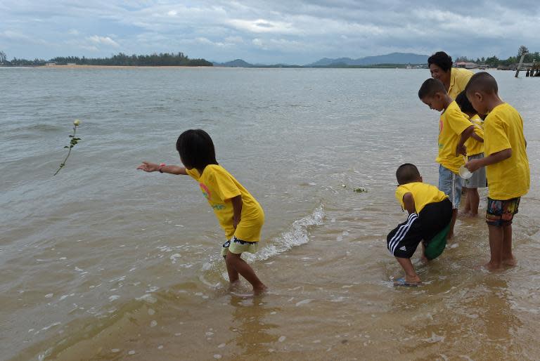 Thai children throw roses into the sea near the Ban Nam Khem tsunami memorial park wall in memory of the victims of the disaster in Phang-nga province