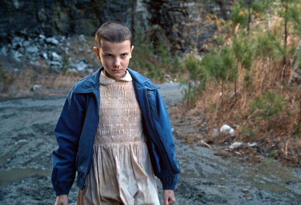 young teen girl with a shaved head and bloody nose standing outside