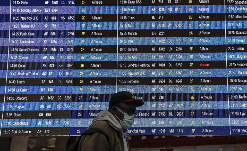 Passenger wearing a face mask walk past a flight information board at Paris' Charles de Gaulle international airport in Roissy, Monday Dec. 21, 2020. France is banning all travel from the U.K. for 48 hours in an attempt to make sure that a new strain of the coronavirus in Britain doesn't reach its shores. (AP Photo/Lewis Joly)