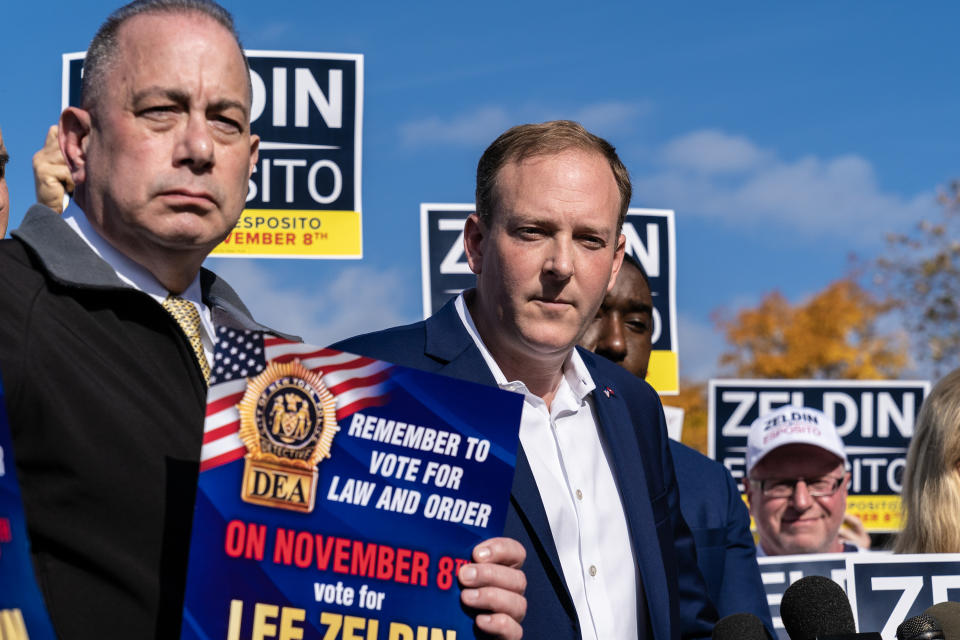 Lee Zeldin with a supporter carrying a poster saying: Remember to Vote for Law and Order on November 8th, vote for Lee Zeldin.