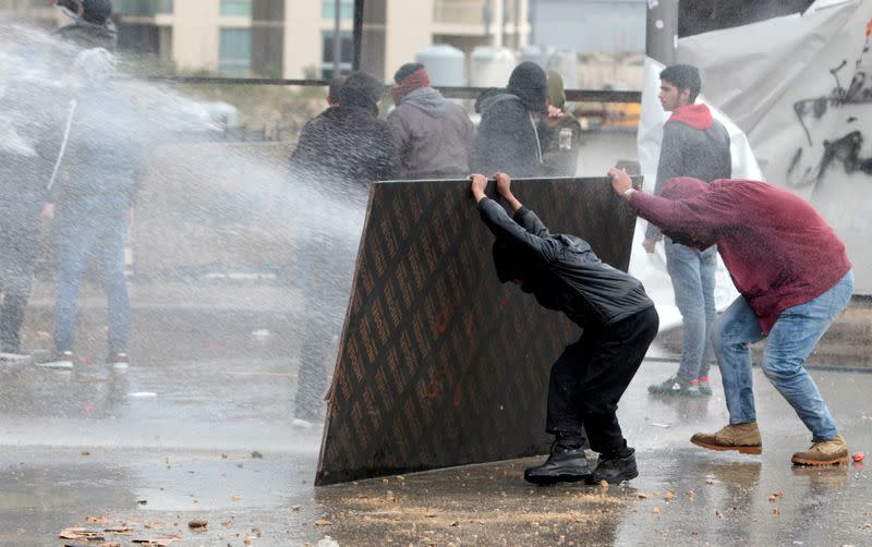 Demonstrators take cover from water cannon during a protest seeking to prevent MPs and government officials from reaching the parliament for a vote of confidence, in Beirut