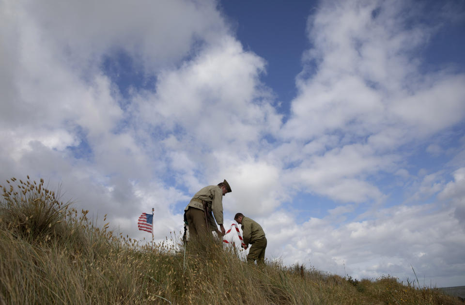 Two men in WWII period uniforms mark off an area in a dune overlooking Omaha Beach prior to a ceremony at the Charles Shay Memorial in Saint-Laurent-sur-Mer, Normandy, France, Friday, June 5, 2020. Saturday's anniversary of D-Day will be one of the loneliest remembrances ever, as the coronavirus pandemic is keeping almost everyone away, from government leaders to frail veterans who might not get another chance for a final farewell to their unlucky comrades. (AP Photo/Virginia Mayo)