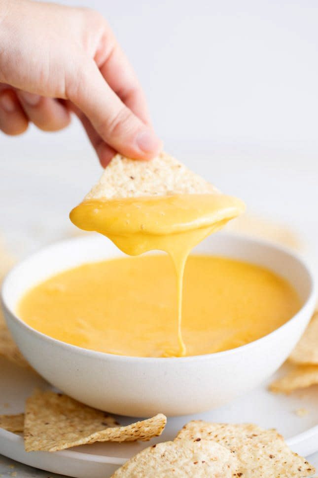 A tortilla chip is dipped in vegan cheese. 