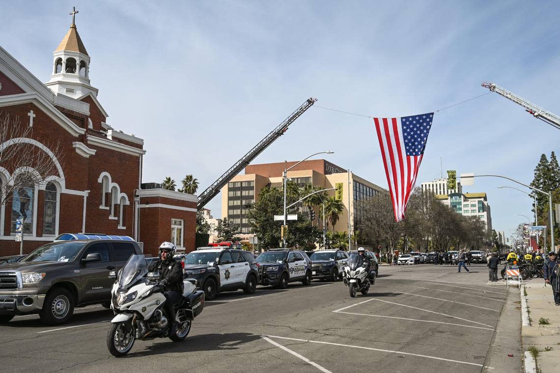 Fresno firefighters hang an American flag across M Street in downtown Fresno as officers from around the state begin lining up to escort fallen Selma officer Gonzalo Carrasco Jr. to Reedley for burial following his funeral service at Selland Arena on Thursday, Feb. 16, 2023.