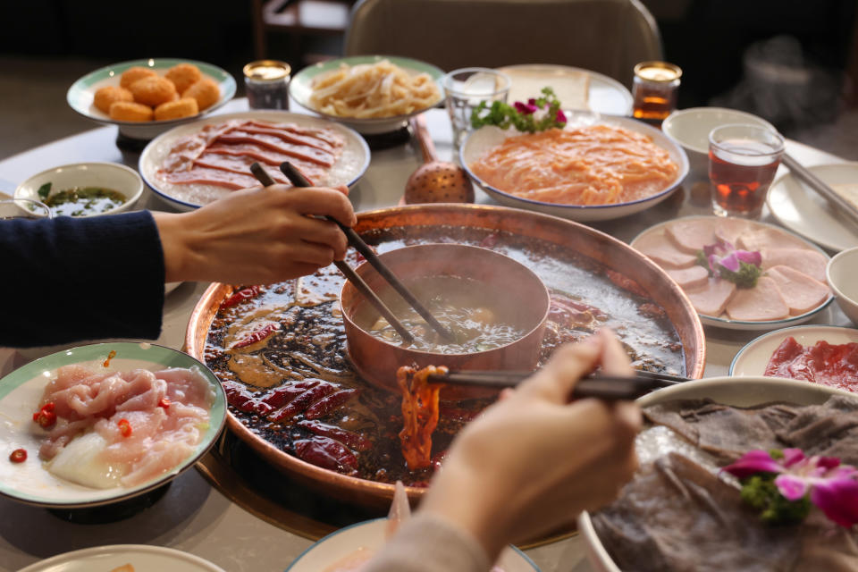 table of hotpot with people taking meat from the bowl