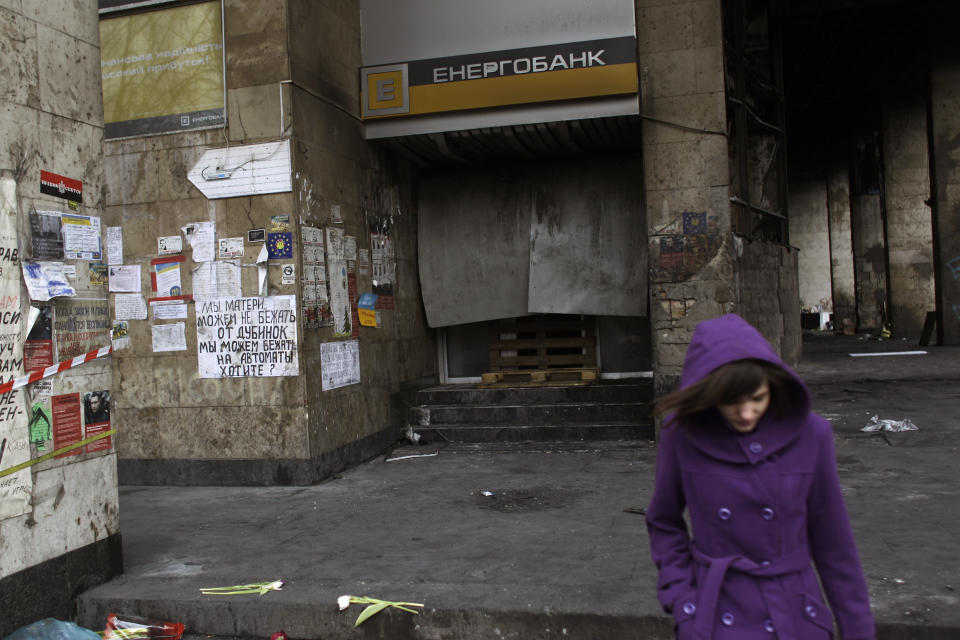 A woman walks past a local bank set on fire in Kiev's Independence Square, the epicenter of the country's current unrest, Ukraine, Tuesday, Feb. 25, 2014. Ukraine needs money, and fast _ in weeks, not months. But bailing out the country of 46 million people will not be as easy as simply writing a big check. For one, Ukraine has already burned the main international financial rescuer, the International Monetary Fund, by failing to keep to the terms of earlier bailouts from 2008 and 2010. Now it needs help again, and its economic and financial problems are worse than before. (AP Photo/Marko Drobnjakovic)