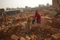 A Syrian woman holds a child next to ancient Roman era ruins where they have set their tents in Sarmada district, north of Idlib city, Syria, Thursday, Nov. 25, 2021. Row upon row of tents, brick homes and other structures with water tanks on top dot the town of Sarmada near the border with Turkey, making up a series of huge informal refugee camps. Women cook, children play, men go to work, pray and discuss politics. Most of the inhabitants are displaced from various bouts of violence in Syria's 10-year conflict. (AP Photo/Francisco Seco)