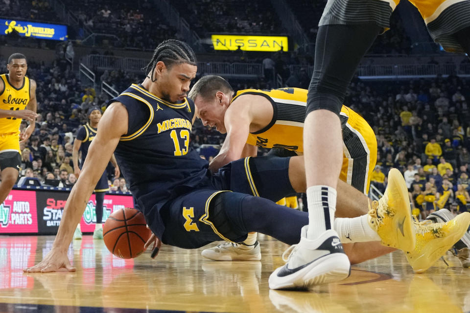 Michigan forward Olivier Nkamhoua (13) falls on the ball as Iowa forward Payton Sandfort (20) reaches in during the second half of an NCAA college basketball game, Saturday, Jan. 27, 2024, in Ann Arbor, Mich. (AP Photo/Carlos Osorio)