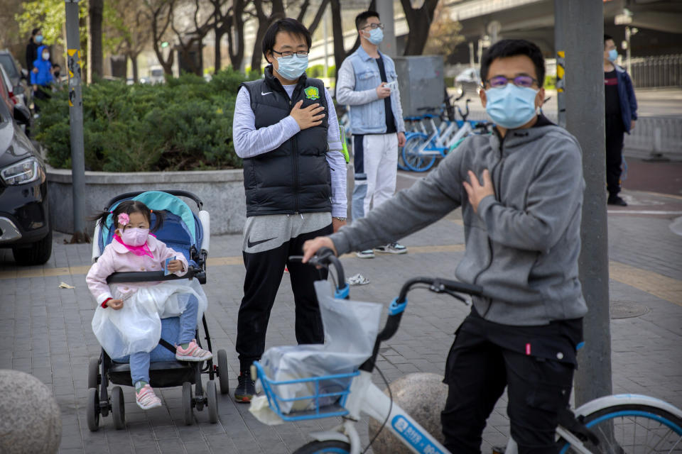 People stand along a street during a national moment of mourning for victims of the coronavirus, in Beijing, Saturday, April 4, 2020. With air raid sirens wailing and flags at half-staff, China on Saturday held a three-minute nationwide moment of reflection to honor those who have died in the coronavirus outbreak, especially "martyrs" who fell while fighting what has become a global pandemic. (AP Photo/Mark Schiefelbein)