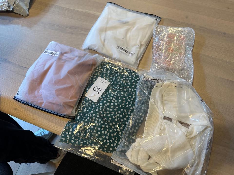 Several transparent plastic bags with garments in them laid out on a wooden table
