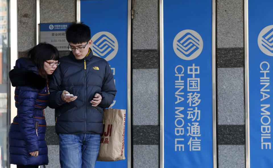 A man uses an Apple iPhone in front of China Mobile banners at one of its branches in Beijing