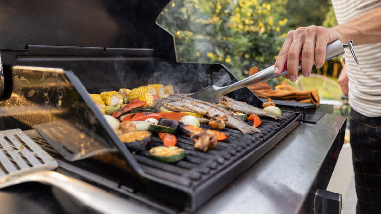 Person grilling fish with vegetables