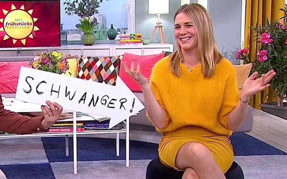 "Schwanger!" ist es auf dem Schild zu lesen, das auf "SAT.1-Frühstücksfernsehen"-Moderatorin Alina Merkau zeigt. Die 34-Jährige erwartet zum zweiten Mal Nachwuchs. (Bild: SAT.1)