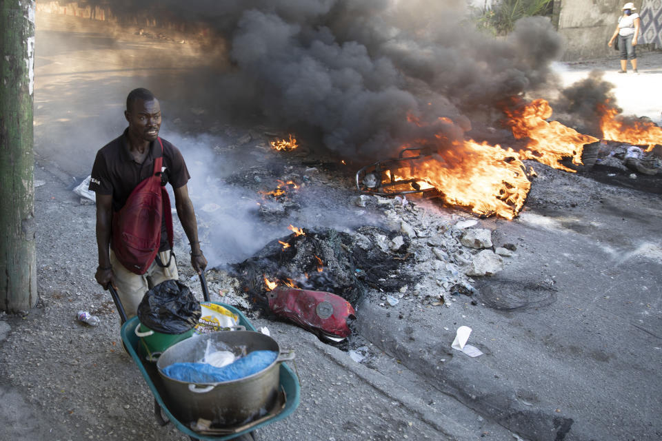 A street vendor pushes his wheelbarrow past burning barricades set up by protesters in reaction to rising fuel prices, in Port-au-Prince, Haiti, Friday, Dec. 10, 2021. (AP Photo/Odelyn Joseph)