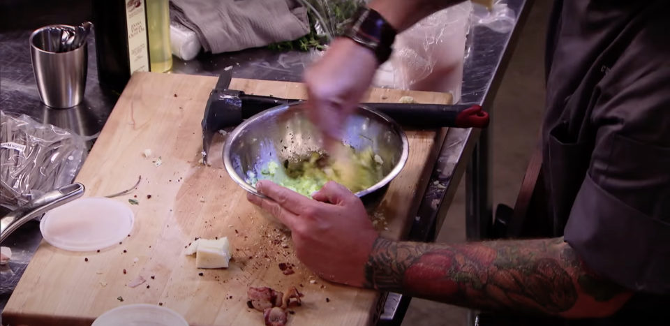 Person mixing ingredients in a bowl on a kitchen counter with tattoos visible on their arm