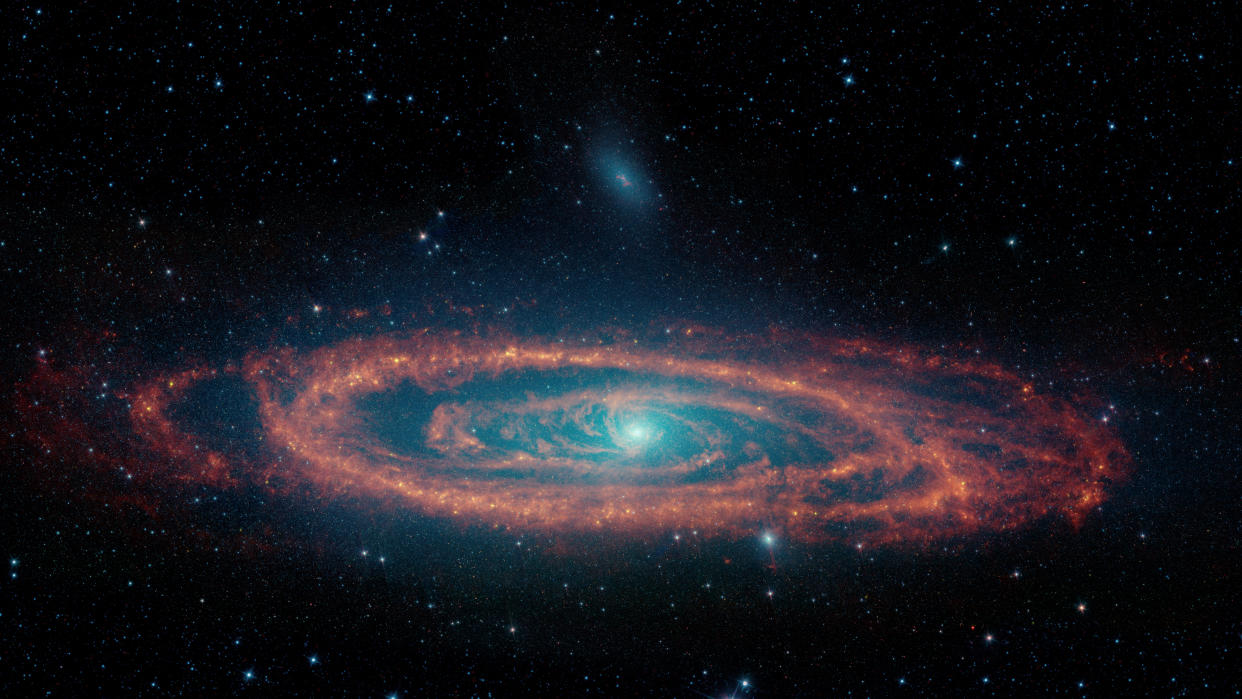  An orange red swirl of gas surrounds the bright shining blue white center of a galaxy in space. 