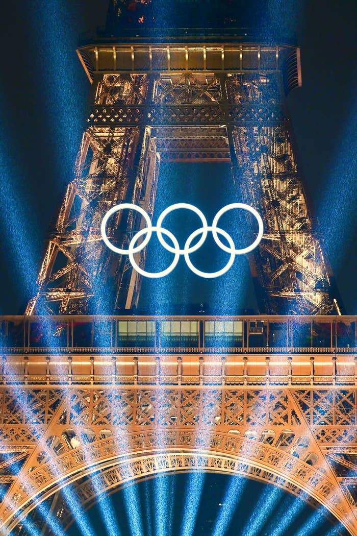 Eiffel Tower illuminated at night, with the Olympic rings in the foreground, symbolizing the upcoming Olympic Games in Paris