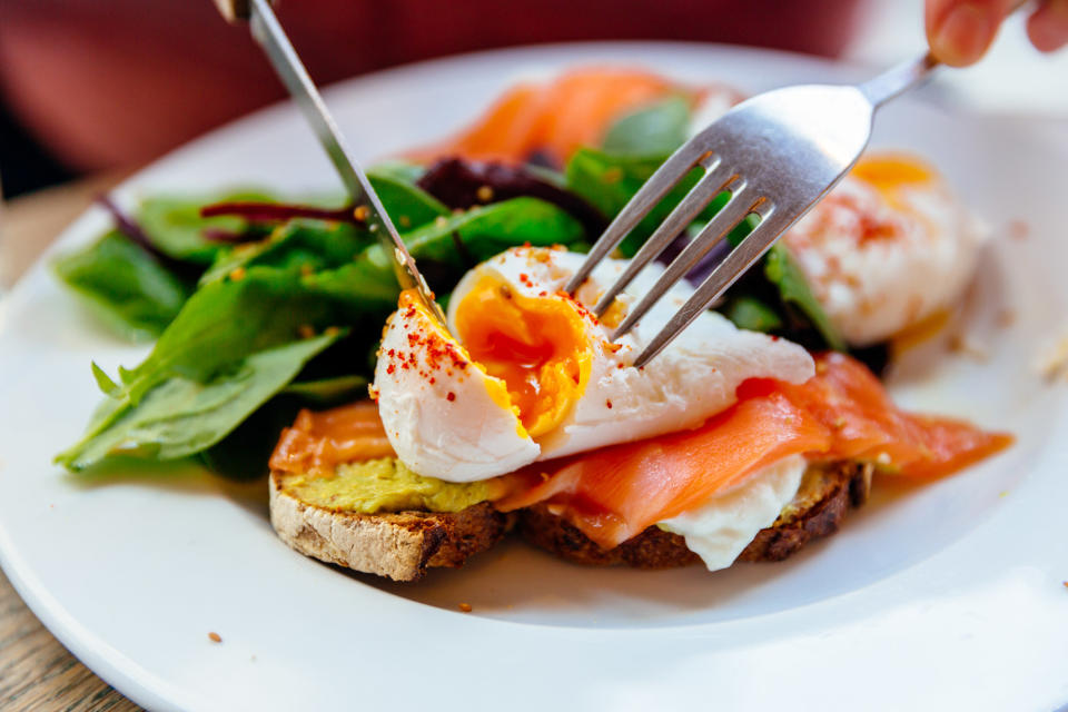 Cutting poached egg on top of avocado toast with salmon.