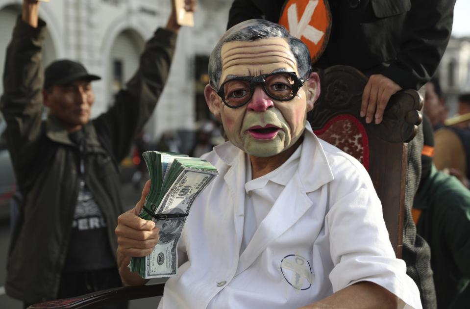 An actor wearing a mask depicting former president Alberto Fujimori performs with fake money during a protest, in Lima, Peru, Wednesday, Oct. 17, 2018. TAn appeals judge has freed Peru's opposition leader Keiko Fujimori a week after she was arrested during a money laundering investigation. (AP Photo/Martin Mejia)