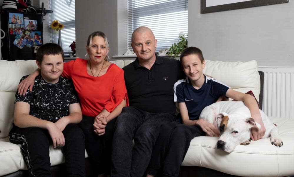 Clare Willsher sits on a sofa next to her husband with their two sons either side and a white dog being held by the boy on the right