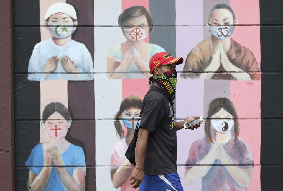 A man wearing a face mask walks past a coronavirus awareness mural depicting children of various faiths praying while wearing face masks in Depok, Indonesia, Wednesday, July 8, 2020. (AP Photo/Dita Alangkara)