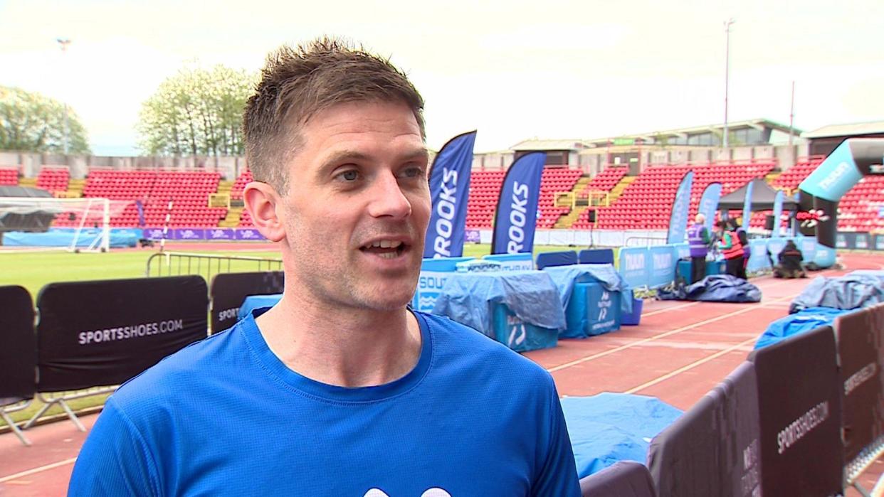 The race organiser at Gateshead stadium with lots of flags behind 