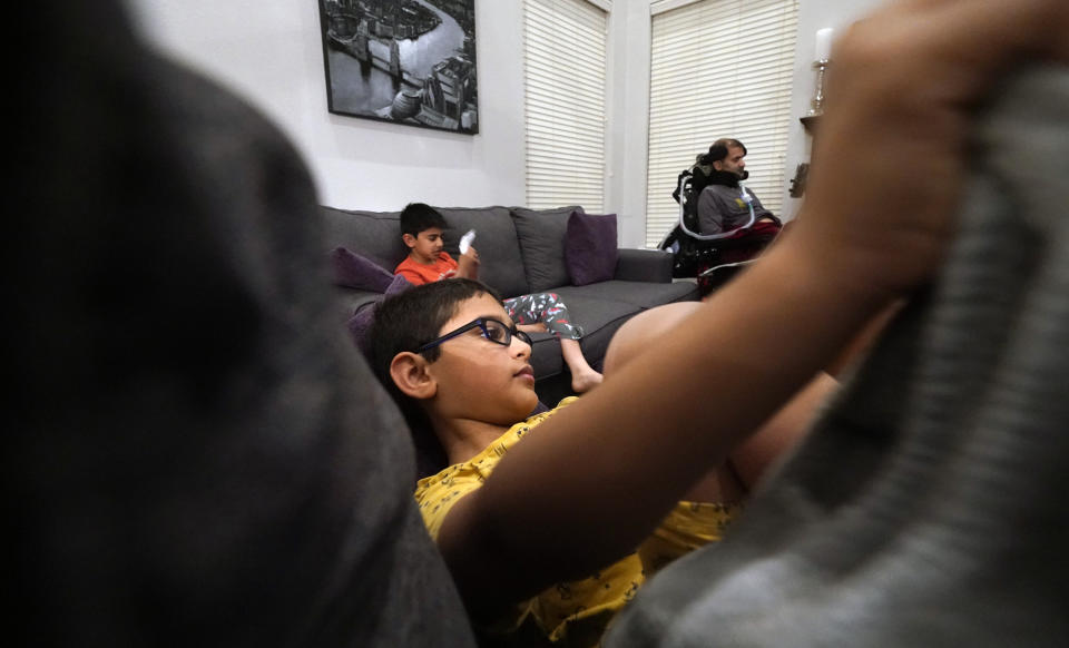 Ronan Kotiya, 11, watches television on the couch with his brother Keaton Kotiya, 9, near their father Rupesh Kotiya in their living room in Plano, Texas, Friday, April 8, 2022. The brother help care for their father who suffers from ALS. (AP Photo/LM Otero)