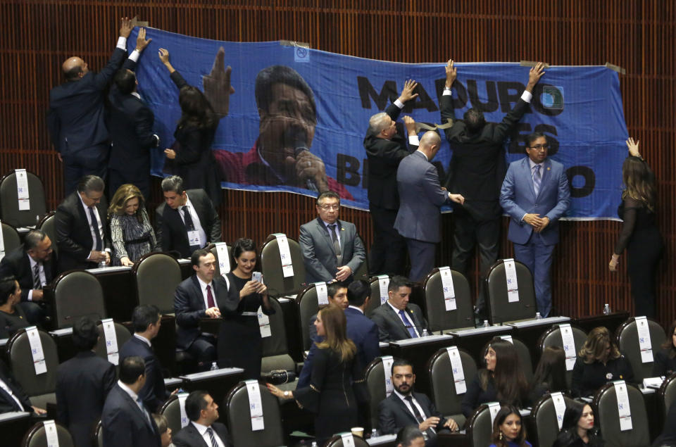 Conservative legislators tape a banner with a message that reads in Spanish: "(Nicolas) Maduro, you're not welcome" to a wall in the lower house of Congress, just a couple of hours before the Venezuelan leader is scheduled to attend the inauguration of President-elect Andres Manuel Lopez Obrador, at the National Congress in Mexico City, Saturday, Dec 1, 2018. Conservative lawmakers voiced objections to Lopez Obrador's decision to invite Maduro to the ceremony. (AP Photo/Marco Ugarte)