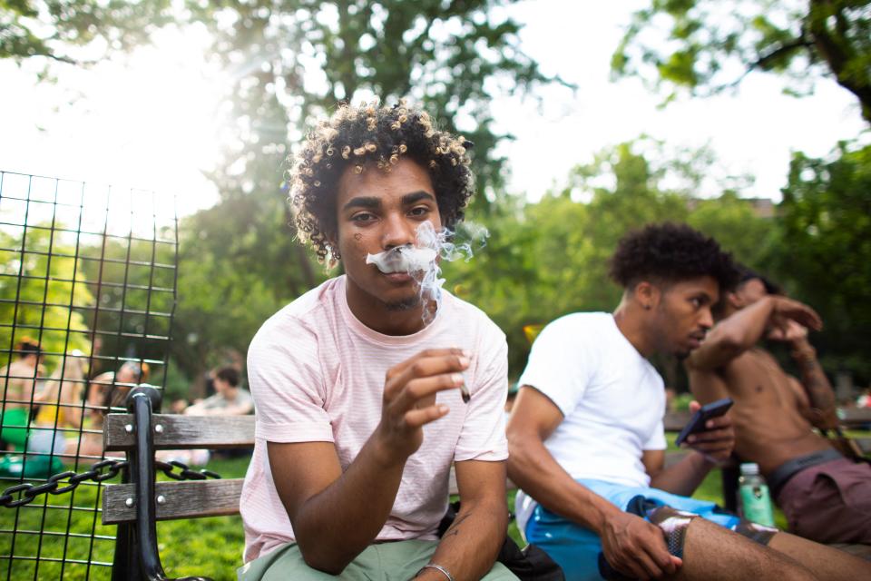 A young man on a park bench smokes marijuana.