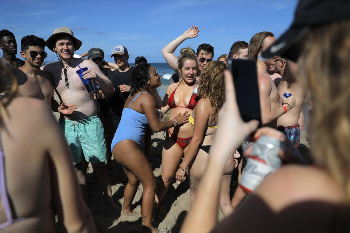 Students in bathing suits and no face masks are tightly packed on a beach