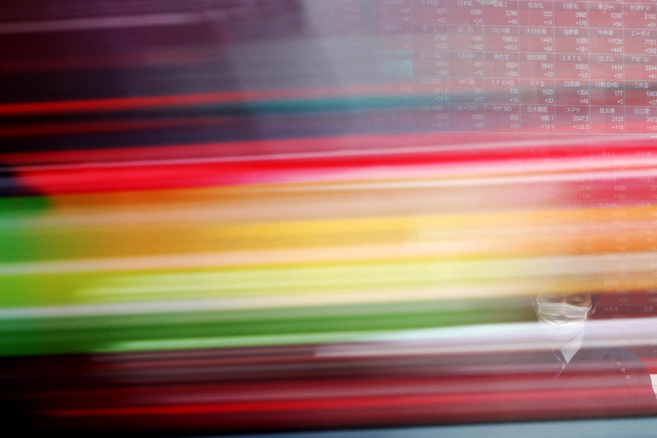 A car drives in front of a man standing near an electronic stock board showing Japan's Nikkei 225 index at a securities firm in Tokyo Friday, March 27, 2020. Shares are mostly higher in Asia after stocks surged again on Wall Street with the approaching approval of a massive coronavirus relief bill by Congress.(AP Photo/Eugene Hoshiko)