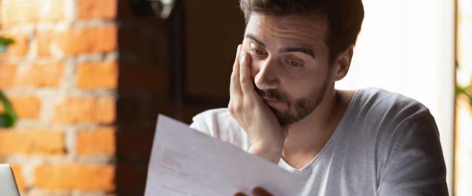 Confused frustrated young man reading mortgage rejection letter in cafe,