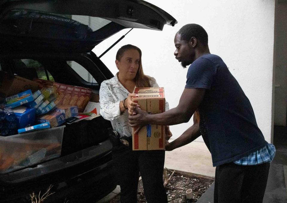 Detective Jennifer Jones of the Riviera Beach Police Department hands a box of food to Jerrick Timmons outside the West Palm Beach Studio 6 Motel on Wednesday.
