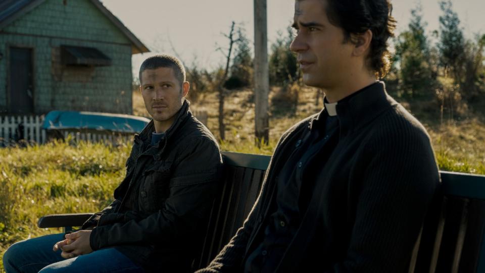 Zach Gilford's Riley and Hamish Linklater's Father Paul chat on a bench with ashen crosses on their head for Ash Wednesday in Midnight Mass.