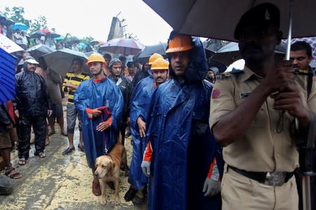Rescue workers look on as others search for survivors after a wall collapased on shanties due to heavy rains at a slum in Mumbai