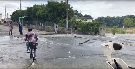 A man cycles on a flooded road damaged after an earthquake hit Osaka, Japan June 18, 2018, in this still image taken from a video obtained from social media. MANDATORY CREDIT. Twitter/@tw_hds/via REUTERS