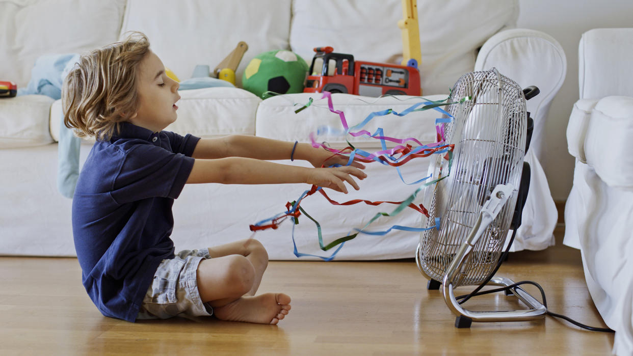 Young boy sitting in front of a fan, desperate for the cool air