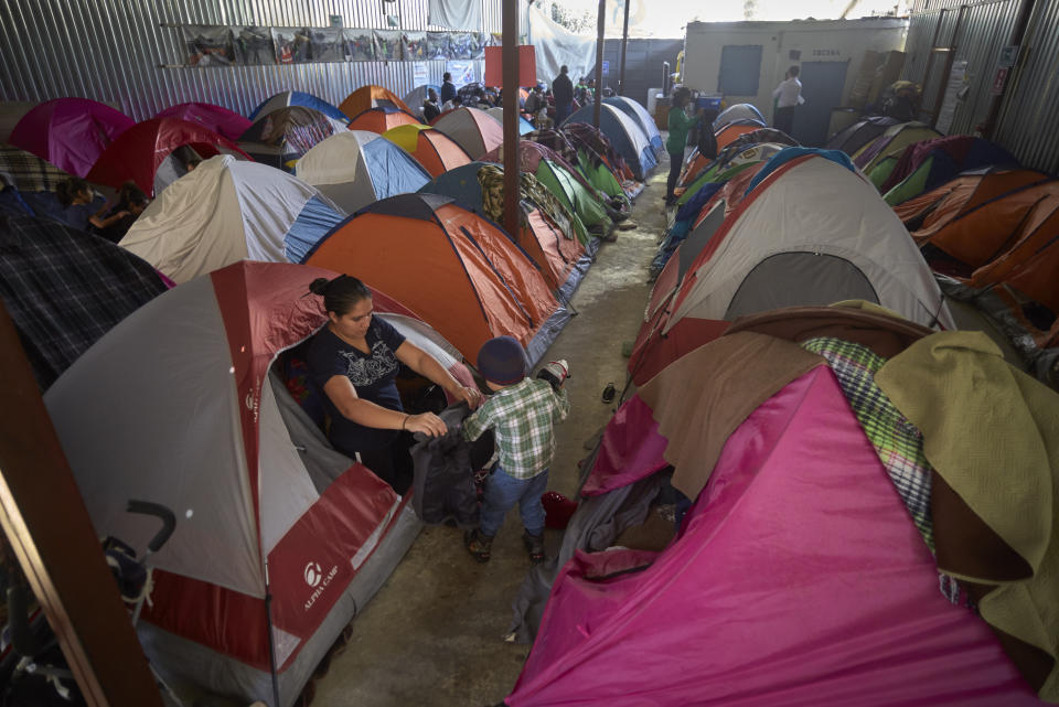 FILE - In this March 5, 2019, file photo, Ruth Aracely Monroy helps her son, Carlos, with his jacket among tents set up inside a shelter for migrants in Tijuana, Mexico. The Perla family of El Salvador has slipped into a daily rhythm in Mexico while they wait for the U.S. to decide if they will win asylum. A modest home replaced the tent they lived in at a migrant shelter. (AP Photo/Gregory Bull, File)