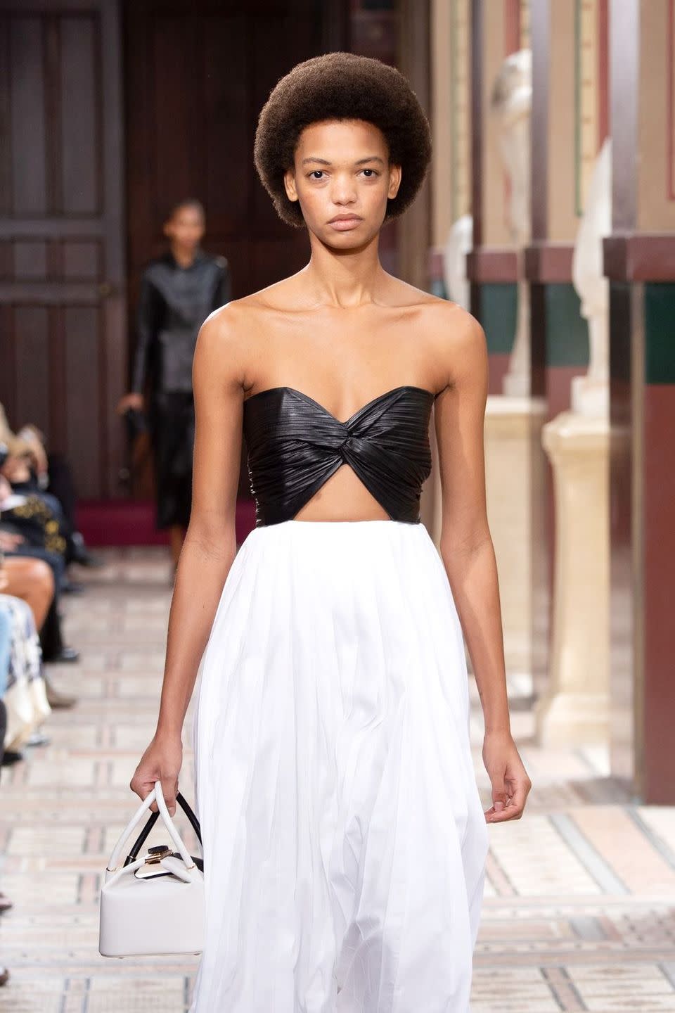 a model wearing a black strapless leather top and a white skirt on the gabriela hearst runway in a roundup of the best strapless bras for small chests 2023