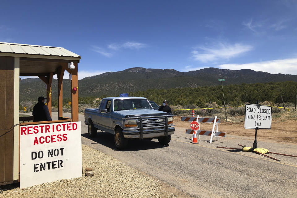 Members of the Native American community of Picuris Pueblo, N.M., including Vaughn Tootsie, right, screen vehicles as they enter and exit tribal property on Thursday, April 23, 2020. Pueblo leaders including Gov. Craig Quanchello see COVID-19 as a potentially existential threat to the tribe of roughly 300 members. The community uses a 24-hour daily roadblock and guardhouse to screen its population for virus symptoms, enforce a ban on nonessential visits and oversee an evening curfew on its members. The pandemic has raged across the nearby Navajo Nation and Zia and San Felipe pueblos. (AP Photo/Morgan Lee)