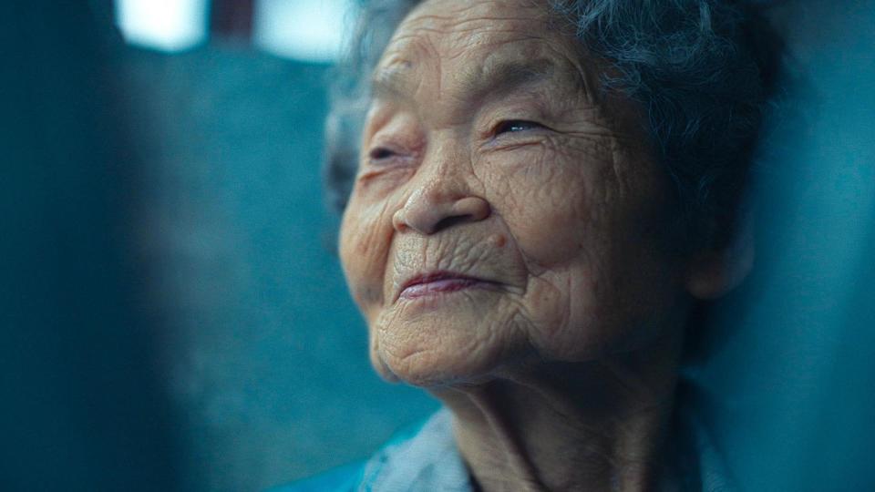 Portrait of Kiyomi Iguro, an elderly woman, looking to the left of the camera, with a small smile on her face. She has short greying hair. 