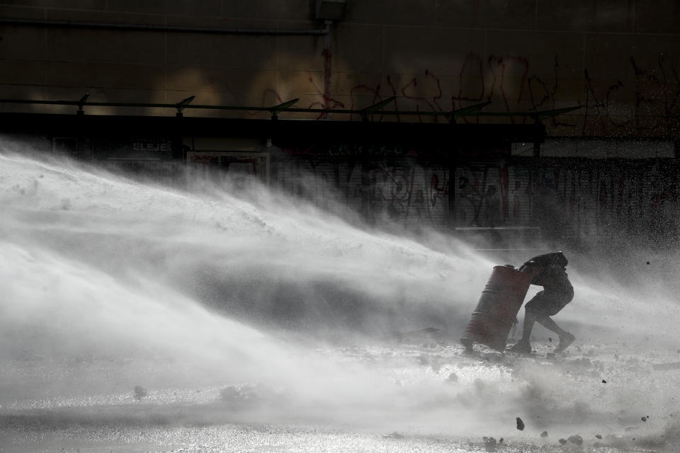 An anti-government demonstrator challenges a police water cannon spray during clashes with police in Santiago, Chile, Thursday, Nov. 14, 2019. Students in Chile began protesting nearly a month ago over a subway fare hike. The demonstrations have morphed into a massive protest movement demanding improvements in basic services and benefits, including pensions, health, and education. (AP Photo/Esteban Felix)