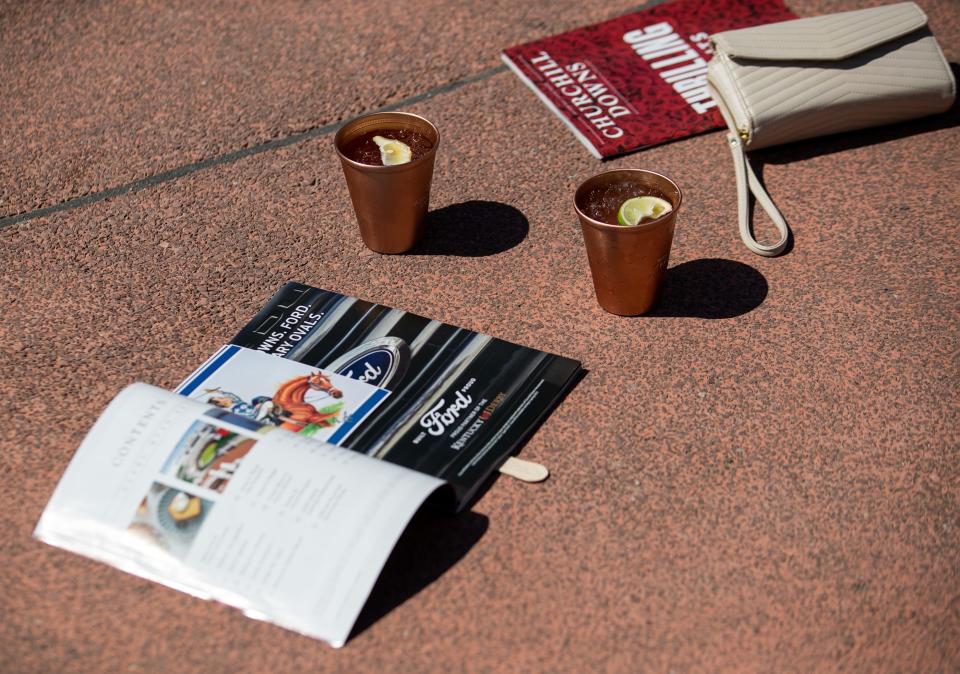 Purses, programs and mint juleps wait on the concrete while people take photos in front of Churchill Downs on Thursday, May 4, 2023