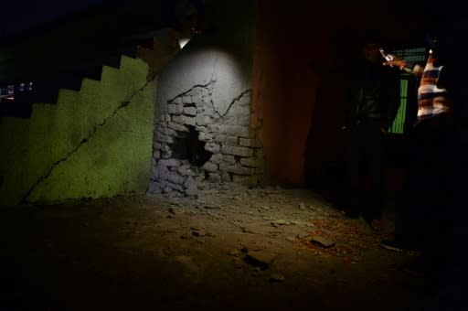 Residents use mobile lights to show what villagers says is a damaged wall by a mortar shell fired from Pakistan, at Kalal village near Nowshera in Jammu region