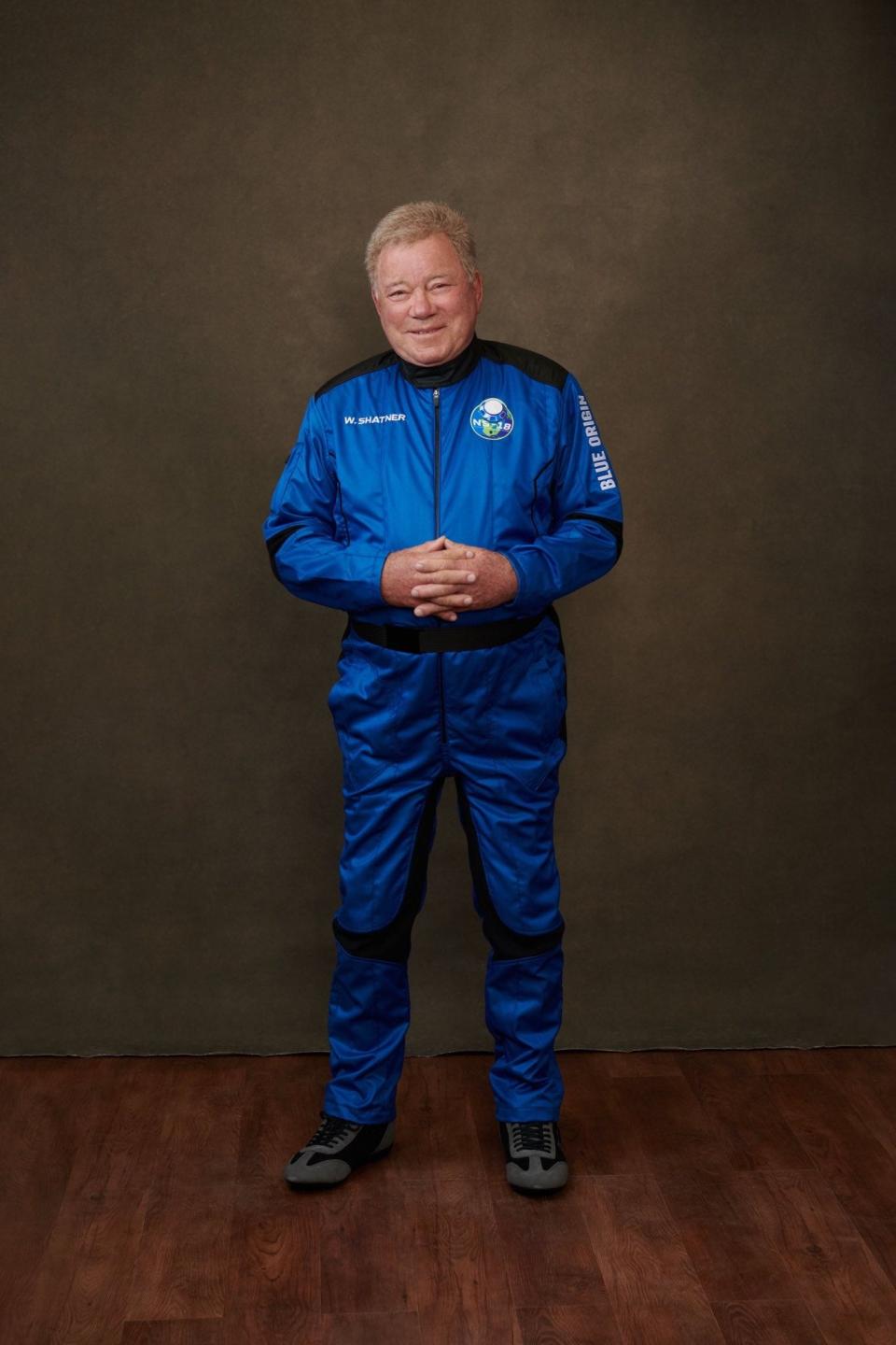 William Shatner smiling in a blue flight suit against grey background