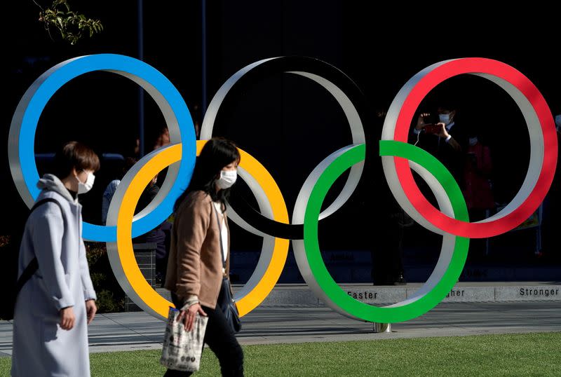 FILE PHOTO: Women wearing protective face masks following an outbreak of the coronavirus disease walk past the Olympic rings in Tokyo