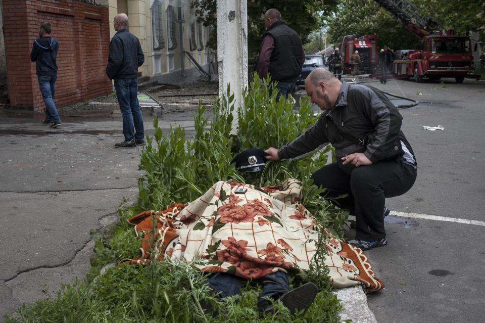 A man looks at the body of a police officer outside a police station in Mariupol, eastern Ukraine, Friday, May 9, 2014. Fighting between government forces and insurgents in Mariupol has left several people dead. (AP Photo/Evgeniy Maloletka)